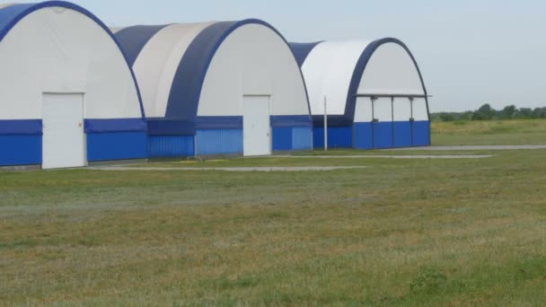 Veduta esterna di una serie di hangar per piccoli aeromobili in un campo d'aviazione fuori città - Filmati, video