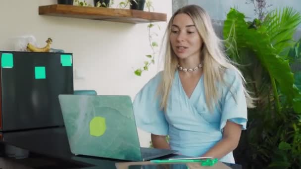 Video of a young girl sitting at a wooden table and working behind a laptop in a green garden - Video, Çekim