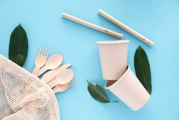 Eco-friendly biodegradable disposable cup and spoon, forks, knives, bamboo tubes, cotton string bag and dishwashing brush on a blue background. Zero waste. Environmental pollution. Place for text. - Photo, Image