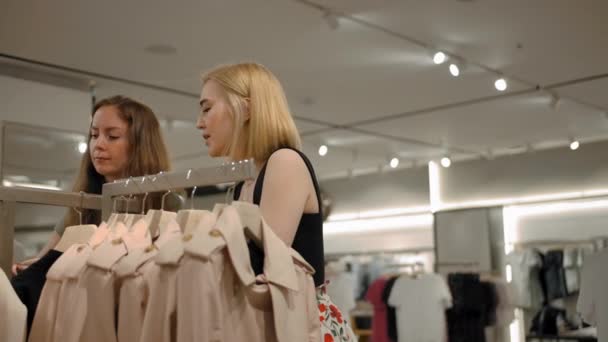Due giovani donne che scelgono vestiti in un negozio di abbigliamento - Filmati, video
