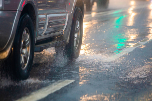 Βρόχινο νερό ροή πιτσιλίσματος από τροχούς του αυτοκινήτου ασήμι κινείται γρήγορα στο φως της ημέρας της πόλης με επιλεκτική εστίαση. - Φωτογραφία, εικόνα