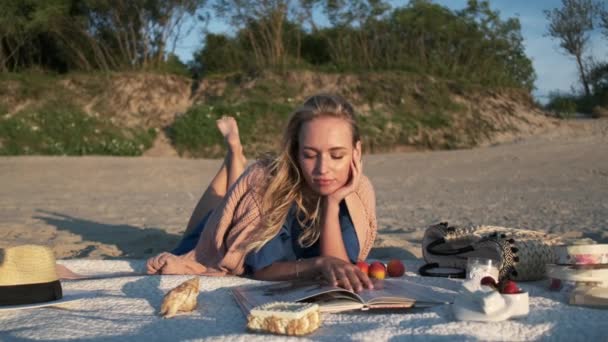 Nuori nainen lukeminen lehden aikana piknik rannalla - Materiaali, video