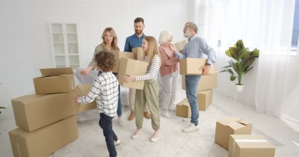 Çocukları ve yaşlıları olan beyaz mutlu bir aile yeni evlerine gelip karton kutu taşıyorlar. Anne, baba, büyükanne, büyükbaba, oğlan ve kız tamirden sonra eve taşınıyorlar. - Video, Çekim