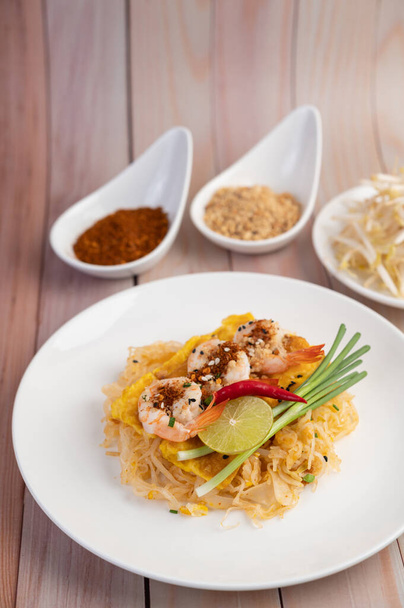 Φρέσκο Pad Thai γαρίδες με lime, μαρούλι, ομελέτα και φρέσκα κρεμμυδάκια σε λευκό πιάτο σε ξύλινο. - Φωτογραφία, εικόνα
