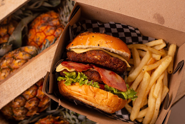 piñas de fondo con una hamburguesa doble de carne y papas fritas en su envase - Foto, imagen