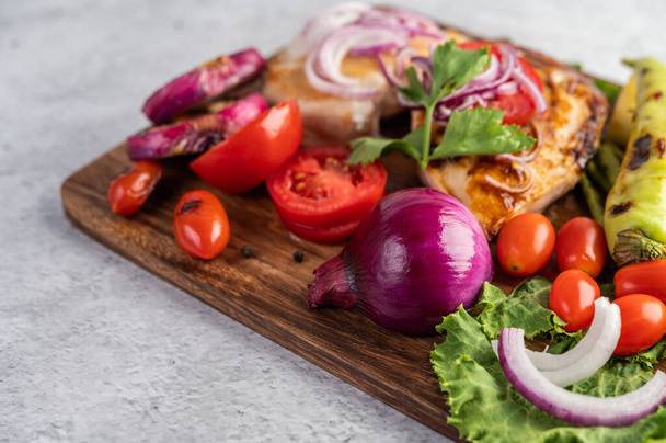 Stek z kurczaka umieszczony na drewnianej tacy z papryką, pomidorami, czerwoną cebulą, sosem ananasowym, sałatą i sezamem - Zdjęcie, obraz