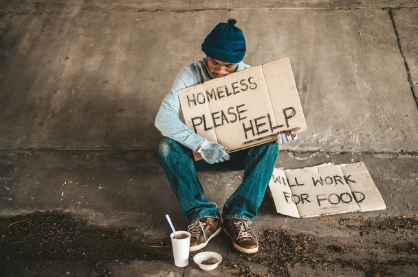 乞食はホームレスのメッセージで橋の下に座っている。助けてください. - 写真・画像