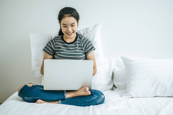 Uma mulher vestindo uma camisa listrada na cama e jogando laptop feliz
. - Foto, Imagem