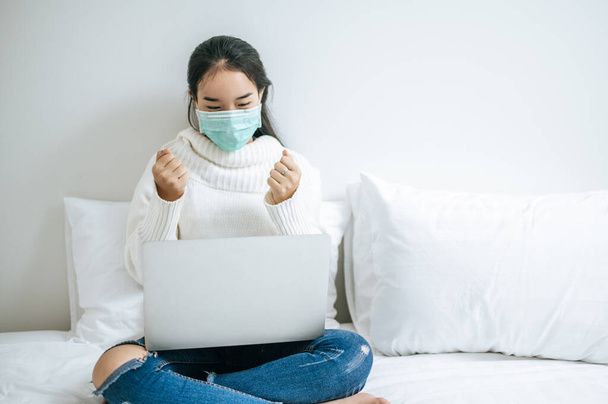 Woman wearing a mask, sitting on the bed and playing laptop. - Photo, Image