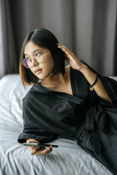 Mulher vestindo uma camisa preta deitada na cama e jogando smartphone
. - Foto, Imagem
