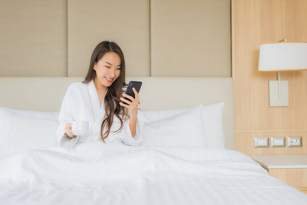 Портрет красива молода азіатка зі смартфоном в інтер'єрі спальні
 - Фото, зображення