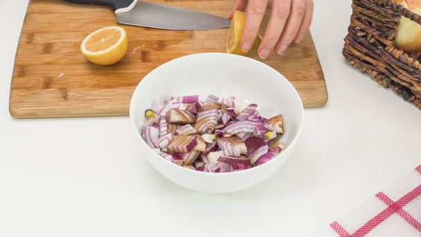 Oignon rouge haché mariné dans un bol sur une table de cuisine blanche. Femme ajoute sauce soja et jus de citron - Photo, image