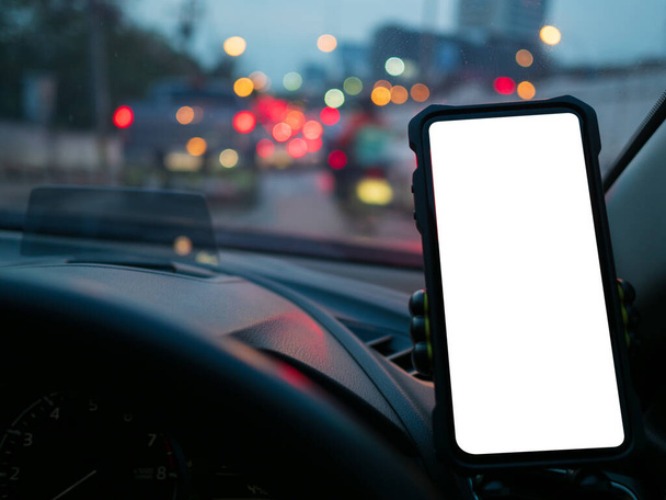 Smartphone o GPS, dispositivo de navegación en un soporte en el coche con fondo borroso de atascos de tráfico por la noche. Mockup pantalla vacía blanca para texto, espacio de copia - Foto, Imagen