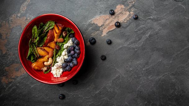Kale salad with caramelized peaches, blueberry and goat cheese, wooden background. Long banner format, top view. - Foto, Bild