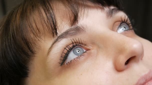Das Gesichtsporträt einer schönen jungen Frau mit blauen Augen und langen Wimpern vor der Prozedur des permanenten Make-up durch Microblading mit Augenbrauen-Tätowierung liegt auf einer Couch in einem Schönheitssalon - Filmmaterial, Video