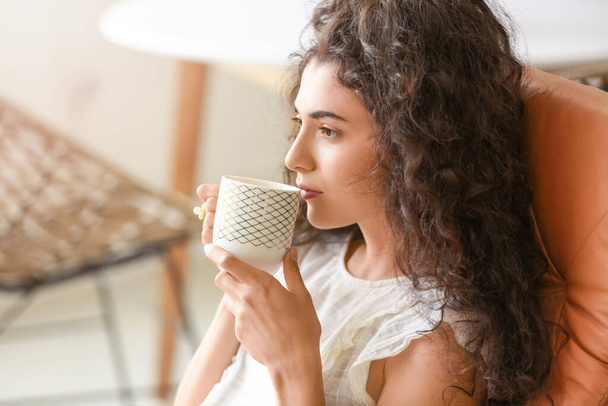 Όμορφη νεαρή γυναίκα πίνει ζεστό τσάι στο σπίτι - Φωτογραφία, εικόνα