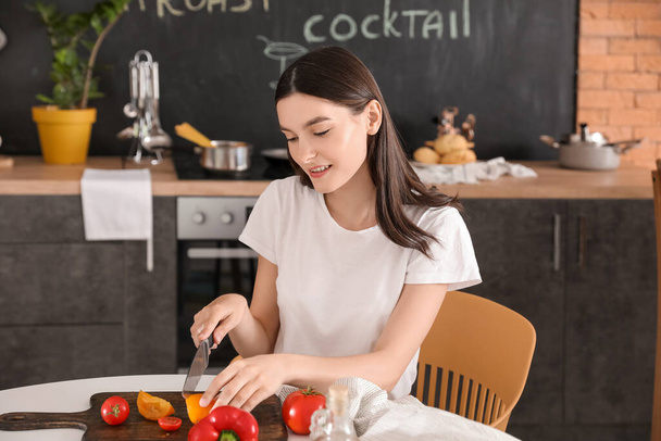 Красивая молодая женщина делает овощной салат на кухне - Фото, изображение
