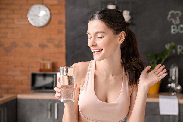 Beautiful young woman drinking water in kitchen - Zdjęcie, obraz