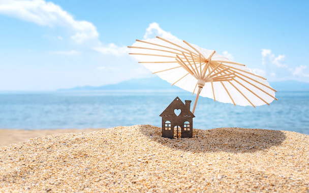 Parapluie et maison sur une plage de sable, ciel bleu et mer en arrière-plan. Investissement dans l'immobilier de villégiature concept. Vacances de rêve en mer. Espace de copie. - Photo, image