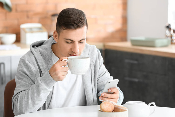 Handsome young man with mobile phone drinking tea at home - 写真・画像
