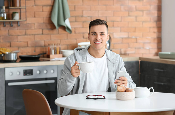 Handsome young man with mobile phone drinking tea at home - Foto, imagen