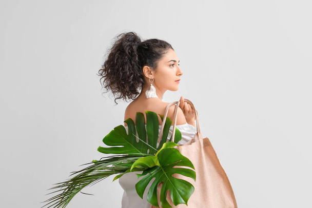 Beautiful young woman with tropical leaves in eco bag on light background - Foto, afbeelding