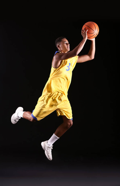Jonge springende Afro-Amerikaanse basketbalspeler op donkere achtergrond - Foto, afbeelding