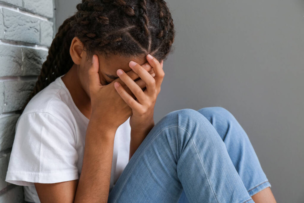Verdrietig Afrikaans-Amerikaans meisje zit naast een grijze muur. Stop racisme - Foto, afbeelding