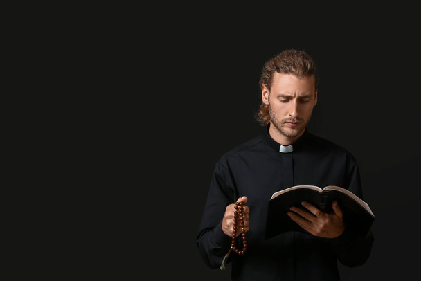 Schöner Priester mit Bibel auf dunklem Hintergrund - Foto, Bild