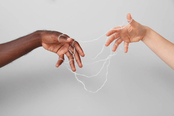 Hände einer kaukasischen Frau und eines afroamerikanischen Mannes mit Stricken auf grauem Hintergrund. Rassismus-Konzept - Foto, Bild