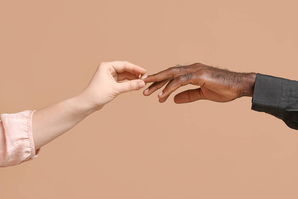 Blanke vrouw zet trouwring om vinger van Afro-Amerikaanse man tegen kleur achtergrond. Racisme - Foto, afbeelding