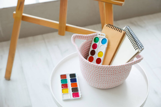 Плетеная корзина с принадлежностями для рисования в комнате
 - Фото, изображение