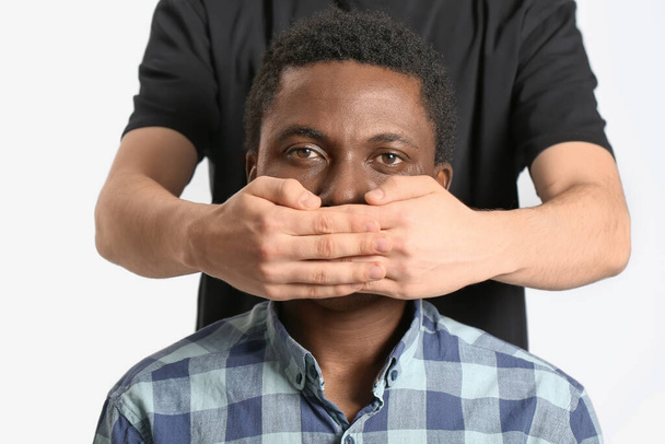 Persona que cubre la boca del triste hombre afroamericano sobre fondo claro. Detener el racismo
 - Foto, Imagen