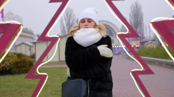 Mujer congelada en sombrero, bufanda, guantes abrazos, se calienta las manos, mira cámara
 - Metraje, vídeo