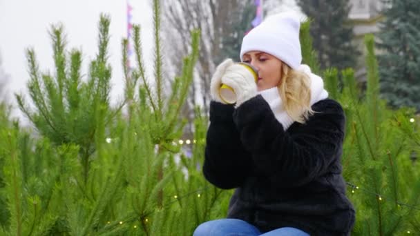 Mujer feliz en sombrero blanco cálido, bufanda, mitones se sienta a beber taza de papel de café
 - Metraje, vídeo
