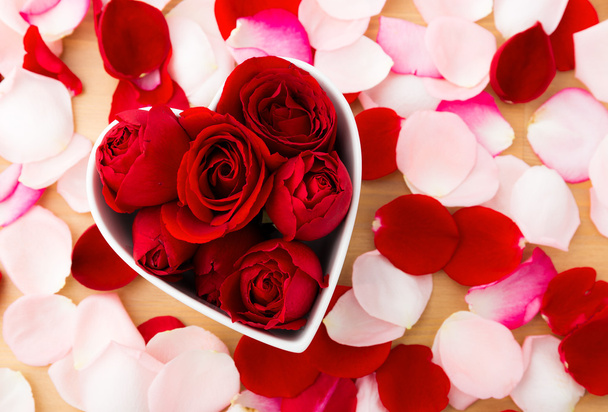 美しい赤いバラ花びらの横にある心臓形状のボウル内 - 写真・画像