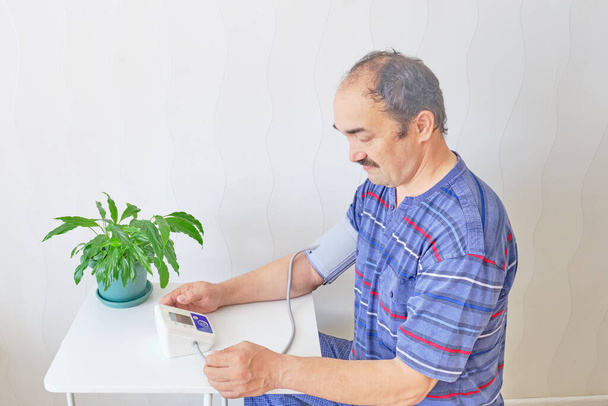 Älterer Mann überprüft Blutdruck zu Hause mit elektronischem Tonometer - Foto, Bild