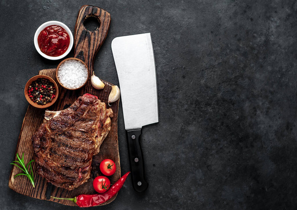 Gegrilde biefstuk met specerijen, groenten en kruiden op een houten snijplank met donkere achtergrond. - Foto, afbeelding