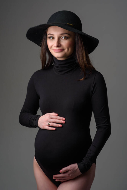 Young beautiful pregnant woman in black bodysuit and hat. - Photo, Image