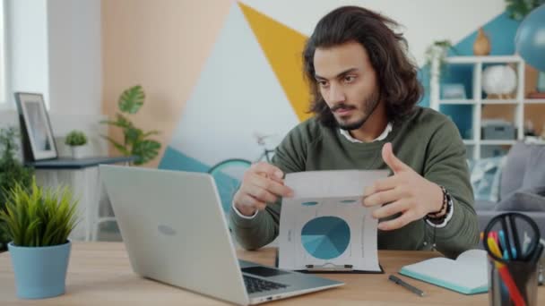 Homem de negócios árabe trabalhando em casa olhando para documentos e usando laptop
 - Filmagem, Vídeo