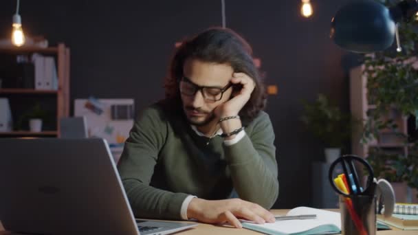 Arabi mies nukkuu toimistossa pöydällä sitten herääminen ja työskentely kannettava tietokone myöhään illalla - Materiaali, video