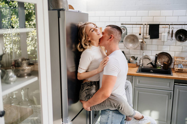 pair of lovers kissing and hugging in kitchen next to the refrigerator. - Photo, image