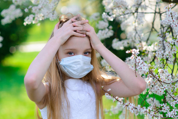 Tiener meisje met medisch masker in de lente bloeiende tuin. Concept sociale afstand, preventie van coronavirus. - Foto, afbeelding