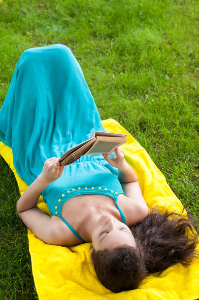 Η Μπρουνέτ είναι ξαπλωμένη στην πλάτη της και διαβάζει βιβλία στο πάρκο. - Φωτογραφία, εικόνα