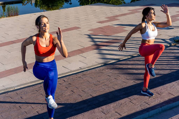 Two young Caucasian athletic female friends doing exercises and stretching outside - healthy lifestyle concept - Photo, image