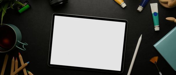 Κάτοψη του mock up digital tablet και stylus σε μαύρο τραπέζι με εργαλεία ζωγραφικής, notebook και κύπελλο   - Φωτογραφία, εικόνα