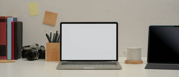 Vista ravvicinata di semplice tavolo di studio con computer portatile modello up, tablet con tastiera, matita, blocco note, macchina fotografica, libri e tazza - Foto, immagini