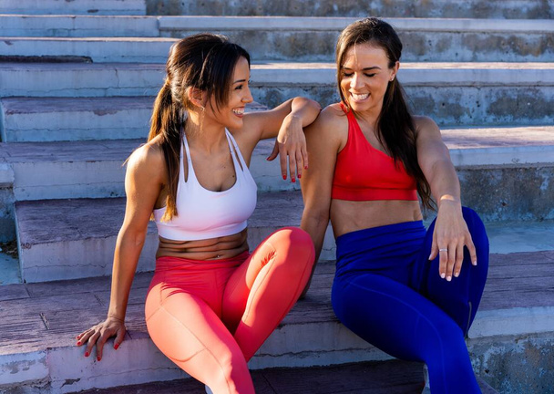 Two young Caucasian athletic female friends sitting on the stairs and talking after a hard workout - Foto, Imagem