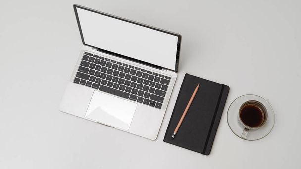 Vista superior do espaço de trabalho simples com laptop simulado, agenda, lápis e xícara de café na mesa branca
  - Foto, Imagem