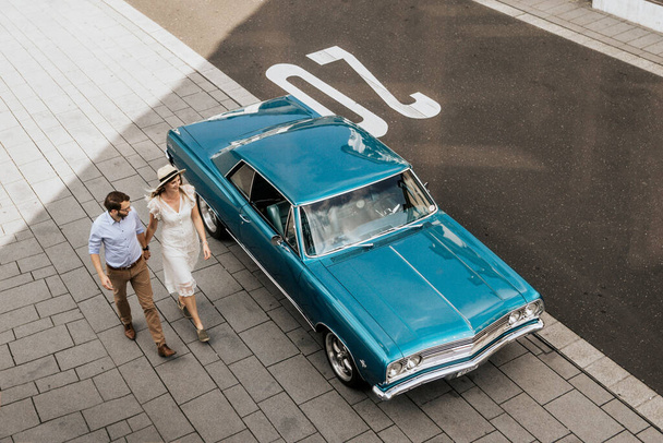 Mavi arabanın yanında yürüyen şık bir çift. Tarz sahibi sevgi dolu aile el ele tutuşur - Fotoğraf, Görsel